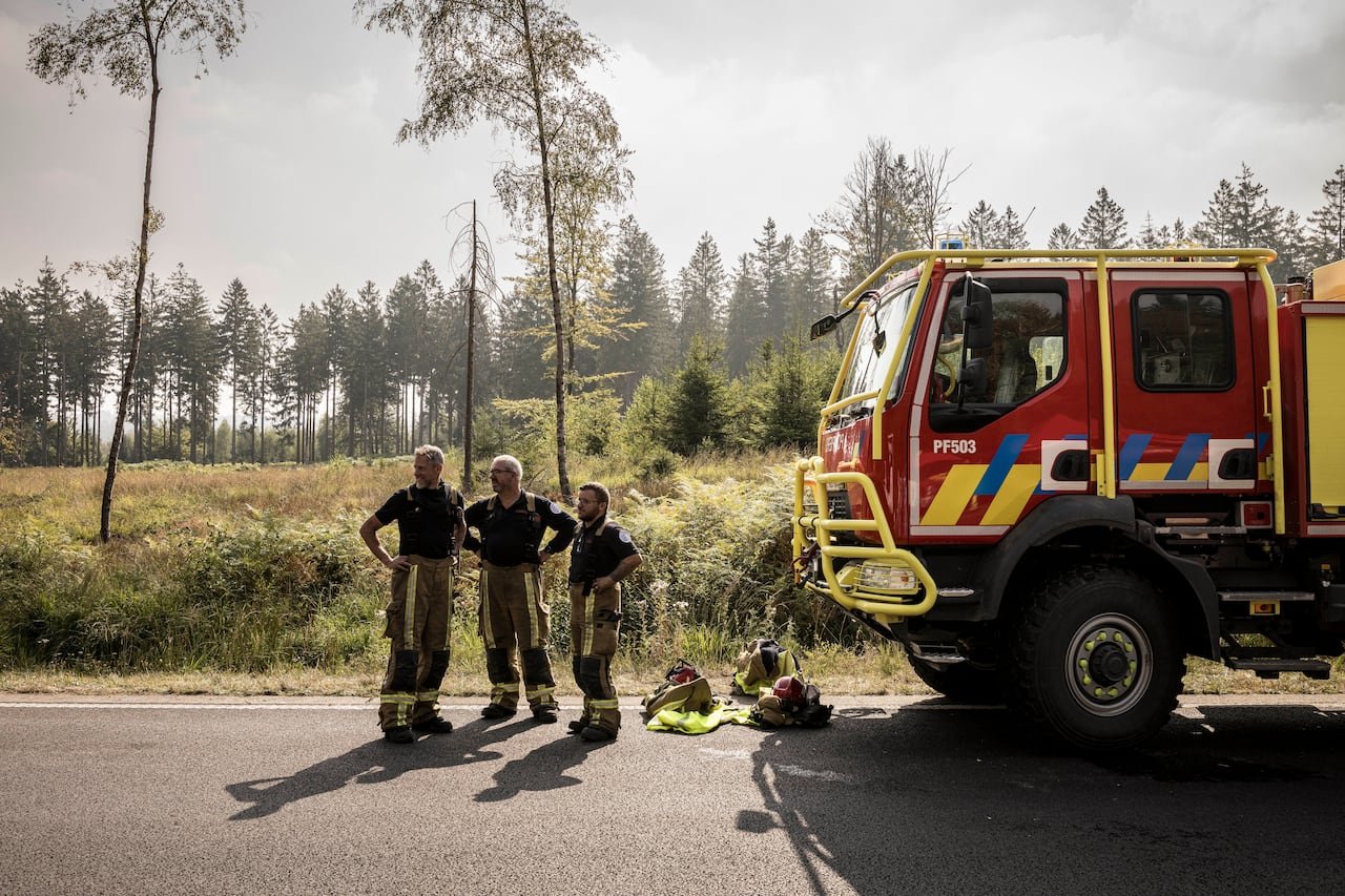 default-238 Three firefighters stand near an emergency car near a wildfire.